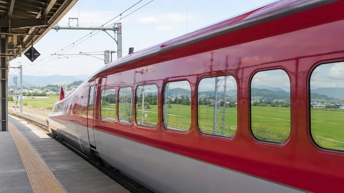 秋田駅ホームで発車を待つ赤い新幹線こまちと車窓に広がる秋田平野の風景