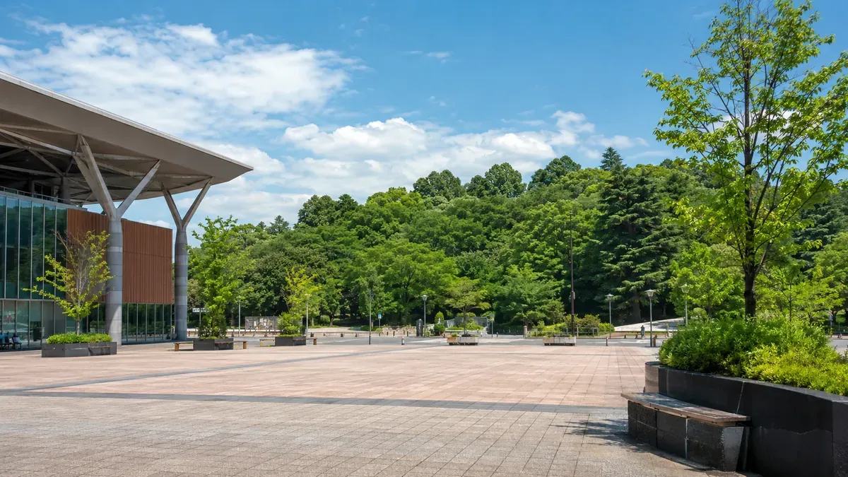夏の秋田駅西口広場から見える、青々と茂る千秋公園の緑と、観光客の姿。