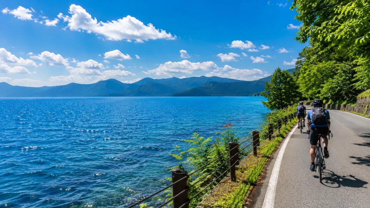 秋田田沢湖のコバルトブルーの湖面、湖畔をサイクリングする人々の夏の風景